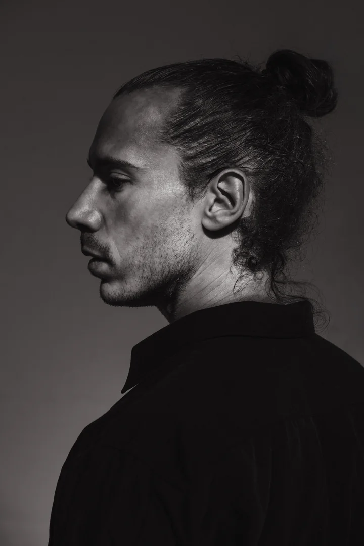 Zeyan Castracane. Close-up profile with hair tied in a bun. Black-and-white studio portrait.