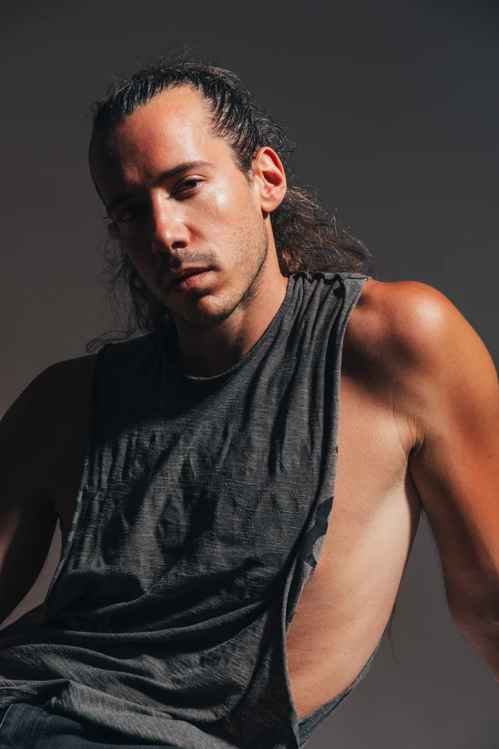 Zeyan Castracane. Close-up in a dark sleeveless top, lit from the side. Colour portrait.