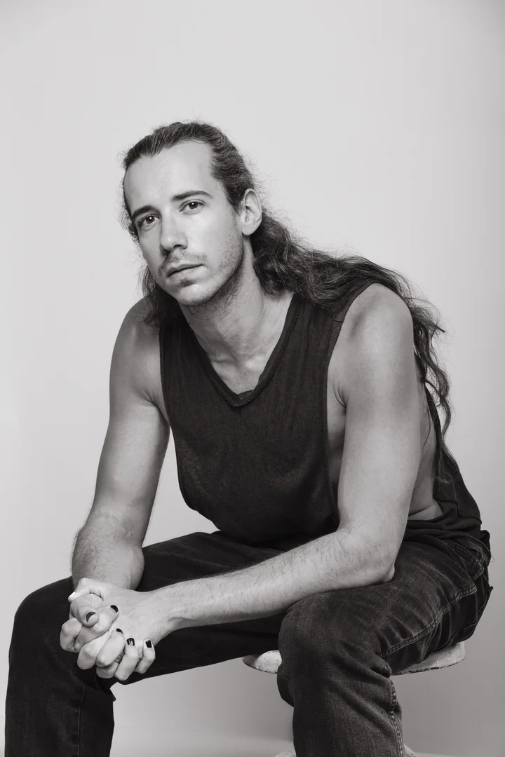 Zeyan Castracane. Leaning forward with hands clasped and long hair tied back. Black-and-white portrait.