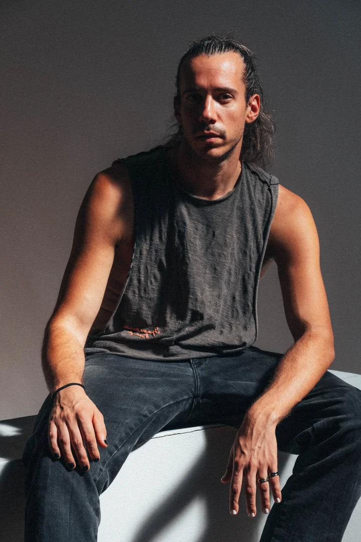 Zeyan Castracane. Seated on a white block with dramatic side lighting. Colour portrait.