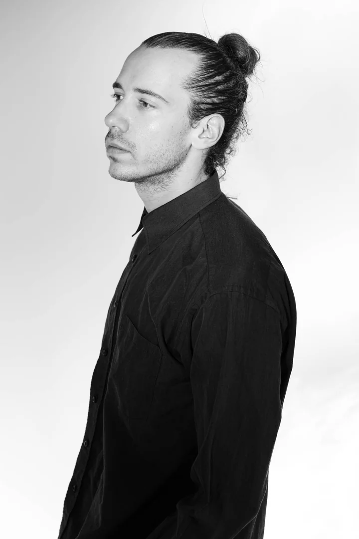 Zeyan Castracane. Turned to the side in a buttoned black shirt. Black-and-white portrait.
