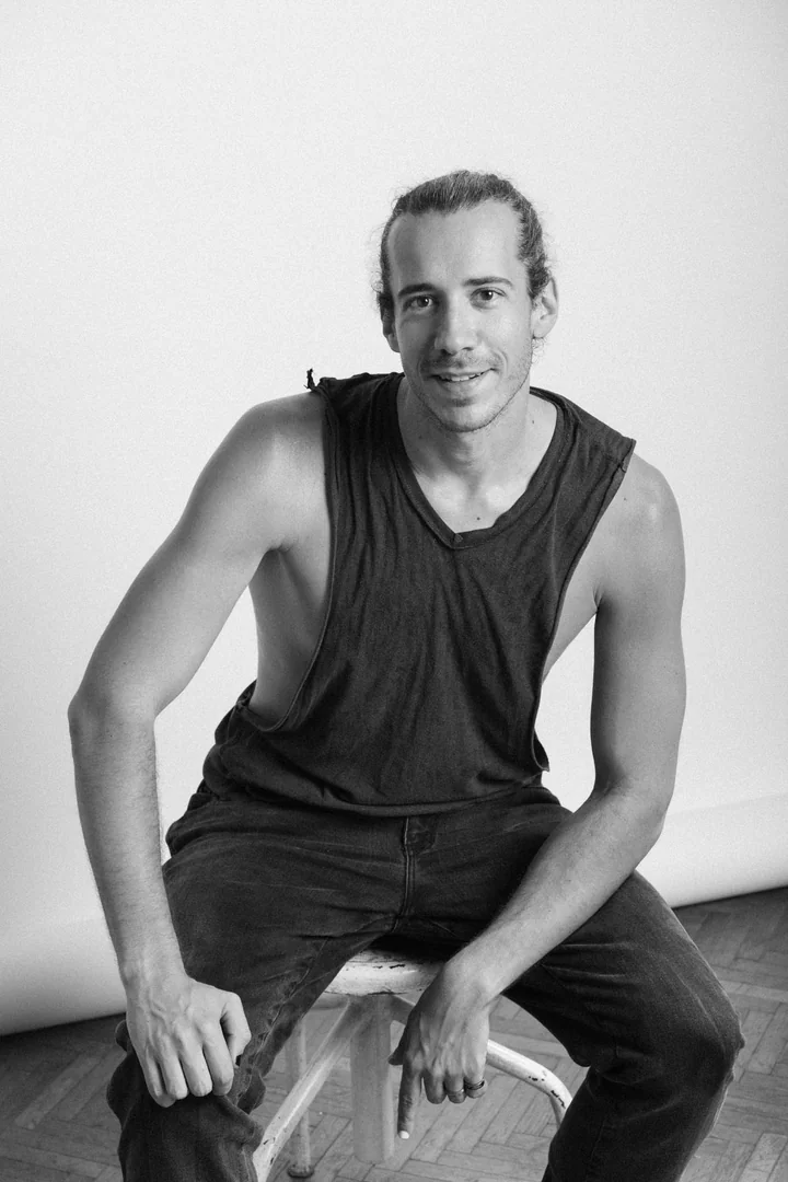 Zeyan Castracane. Smiling while seated on a studio stool. Black-and-white portrait.