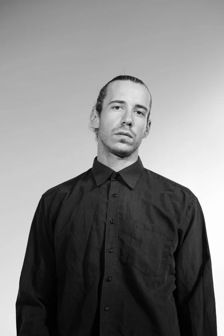 Zeyan Castracane. Standing in a buttoned black shirt. Black-and-white portrait.